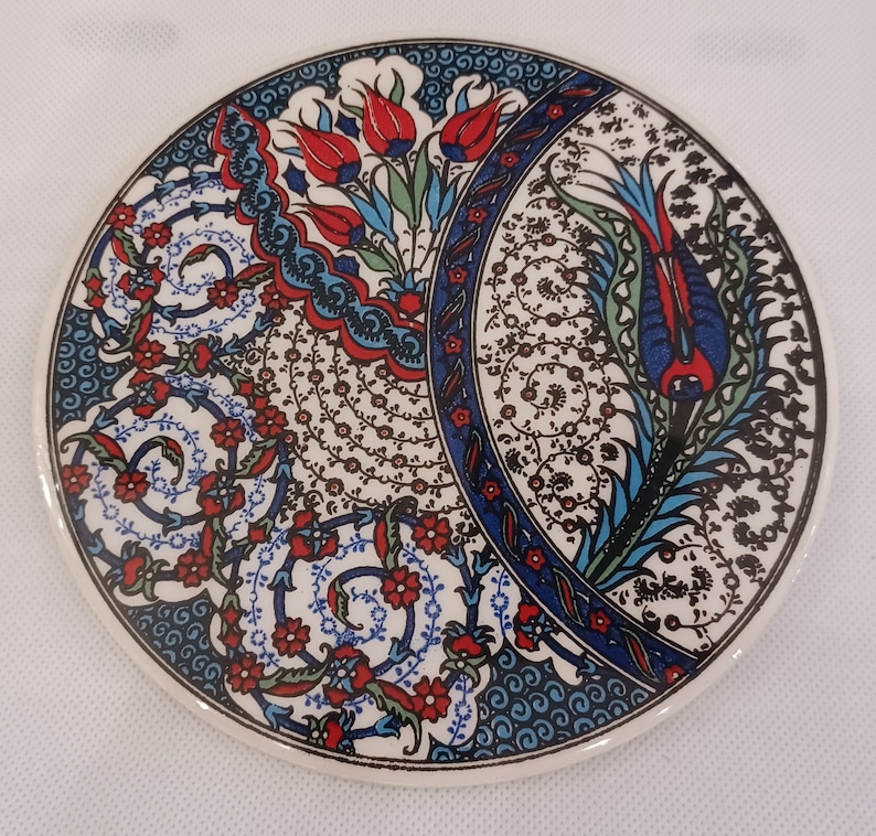 May include: A round ceramic coaster with a blue, white, and red floral pattern. The design features stylized flowers and leaves with intricate details.