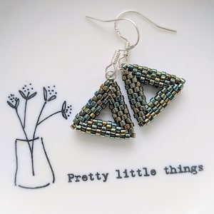 May include: Handmade beaded earrings, triangular in shape, with iridescent green, blue, and gold beads. The earrings hang from silver-coloured ear wires. The earrings are displayed on a white plate with the text "Pretty little things".