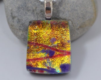 May include: A gold, red, and purple dichroic glass pendant on a silver chain. The pendant is rectangular and has a textured surface.