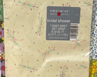 May include: A sheet of bridal shower gift wrap with a light yellow background and a pattern of small pink hearts, purple and green flowers with pink ribbons. The text "Forget Me Not" and "Bridal Shower" is printed in black on a white label. The label also includes the text "1 Giant Sheet Gift Wrap 8.33 sq. ft. (2.5 ft. x 1.1 yd.) American Greetings Corporation Cleveland, Ohio 44144 Made in USA".