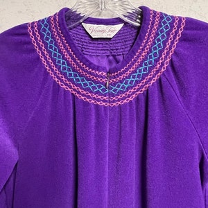 Op de afbeelding: Paarse velours badjas met een roze en blauwe geborduurde halslijn. De badjas heeft een ritssluiting en het label vermeldt "Vanity Fair XS".