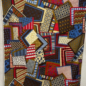 May include: A fabric with a patchwork design featuring various geometric shapes in shades of brown, blue, red, and white. The fabric has a busy, colorful pattern.