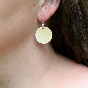 May include: A pair of cream-colored round earrings with silver hooks.