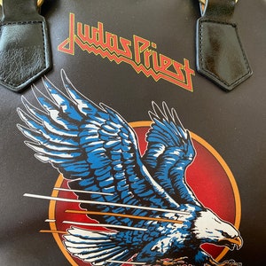 May include: Black leather handbag with a Judas Priest logo and a flying eagle graphic. The eagle is blue, white, and red.