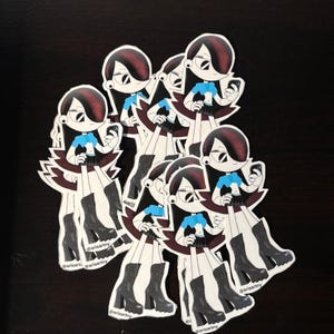 May include: A collection of stickers featuring a cartoon girl with black hair, a blue top, and a black skirt, holding a phone. The stickers have a white border and are layered on a dark surface. The artist's name, @arisartny, is printed on the stickers.