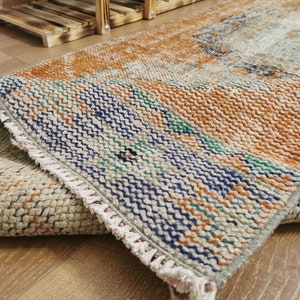 May include: A woven rug with a fringed edge. The rug has a light brown, blue, and green color scheme. The rug is folded in half, showing the pattern on both sides.