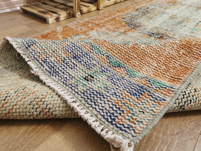 May include: A woven rug with a fringed edge. The rug has a light brown, blue, and green color scheme. The rug is folded in half, showing the pattern on both sides.
