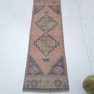 May include: A rectangular, vintage-style rug with a central diamond pattern in shades of peach, blue, and brown. The rug features intricate geometric designs and a fringed edge, suitable for a hallway or entryway.