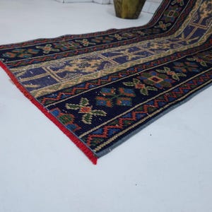 Op de afbeelding: Een rechthoekig, patroonrijk tapijt met een marineblauwe achtergrond en ingewikkelde ontwerpen in beige, rood, groen en blauw. Het tapijt heeft geometrische en bloemmotieven, met een rode rand. Geschikt voor een gang of entree.