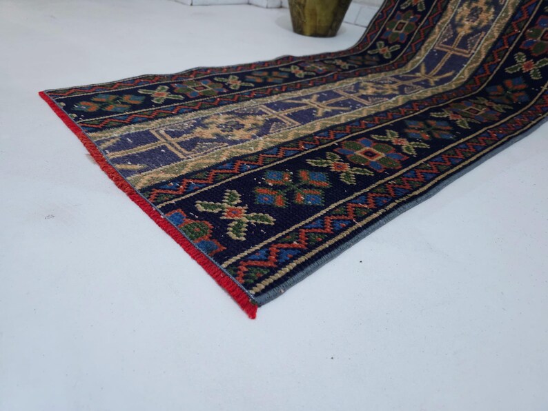 Op de afbeelding: Een rechthoekig, patroonrijk tapijt met een marineblauwe achtergrond en ingewikkelde ontwerpen in beige, rood, groen en blauw. Het tapijt heeft geometrische en bloemmotieven, met een rode rand. Geschikt voor een gang of entree.