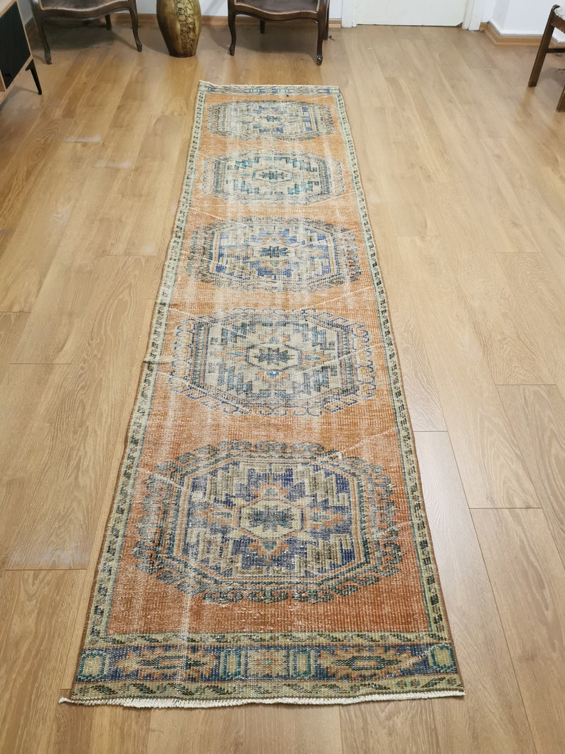 May include: A long, rectangular rug with a faded orange background and a blue and white geometric pattern. The rug has a fringed edge.