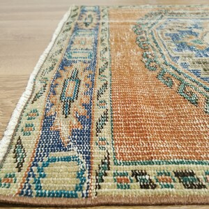 May include: A vintage rug with a brown, beige, blue and green geometric pattern. The rug has a fringe border.