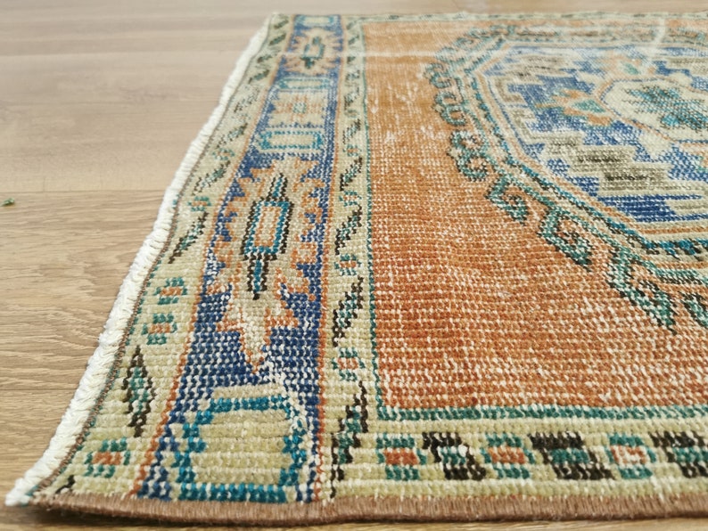 May include: A vintage rug with a brown, beige, blue and green geometric pattern. The rug has a fringe border.