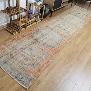 May include: A vintage runner rug with an orange, beige, and blue pattern. The rug has a distressed look and features a floral design.