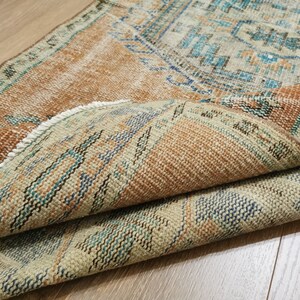 May include: A vintage rug with a brown, beige and blue geometric pattern. The rug is folded in half, showing the intricate details of the woven design.