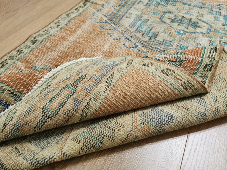 May include: A vintage rug with a brown, beige and blue geometric pattern. The rug is folded in half, showing the intricate details of the woven design.