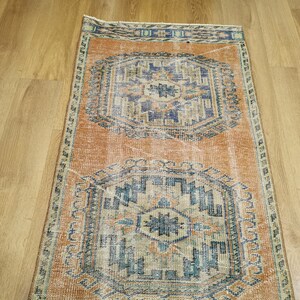 May include: A vintage rug with a faded orange background and intricate blue and beige patterns. The rug has a worn, distressed look, adding to its charm.