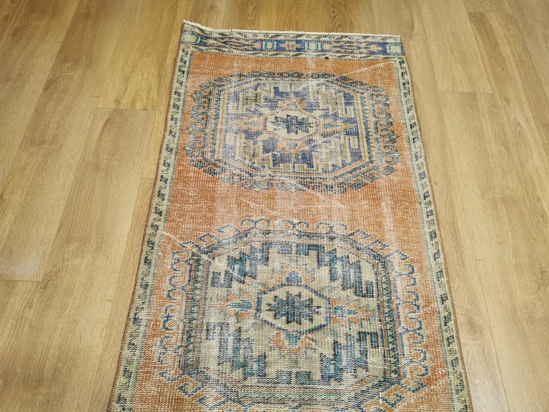 May include: A vintage rug with a faded orange background and intricate blue and beige patterns. The rug has a worn, distressed look, adding to its charm.