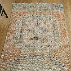 May include: A vintage rug with a faded orange, blue, and white pattern. The rug has a central medallion with a floral design and a distressed look.