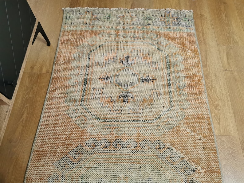 May include: A vintage rug with a faded orange, blue, and white pattern. The rug has a central medallion with a floral design and a distressed look.