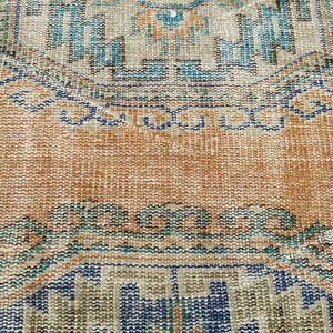 May include: A close-up of a vintage rug with a faded orange background and intricate blue and brown patterns. The rug has a worn and distressed look, adding to its character.