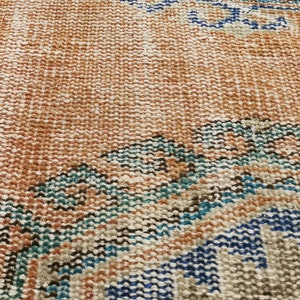 May include: A close-up of a woven rug with a brown, beige, blue, and teal pattern. The rug has a distressed look and is made of natural fibres.