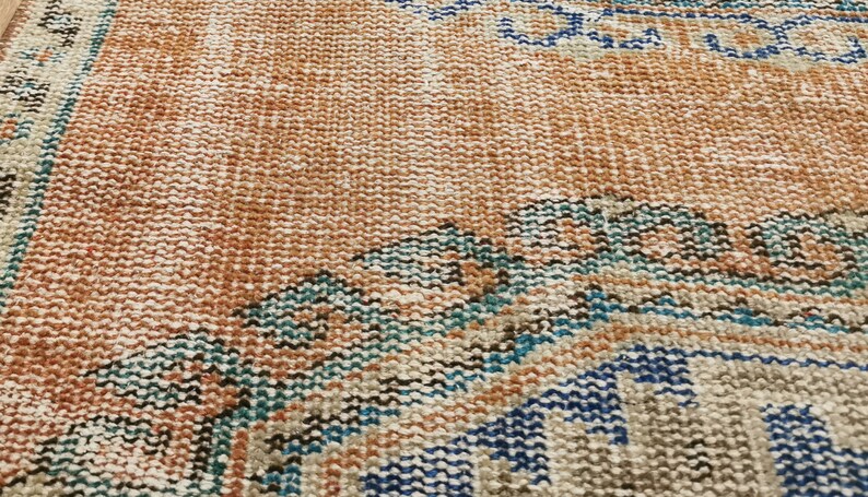 May include: A close-up of a woven rug with a brown, beige, blue, and teal pattern. The rug has a distressed look and is made of natural fibres.