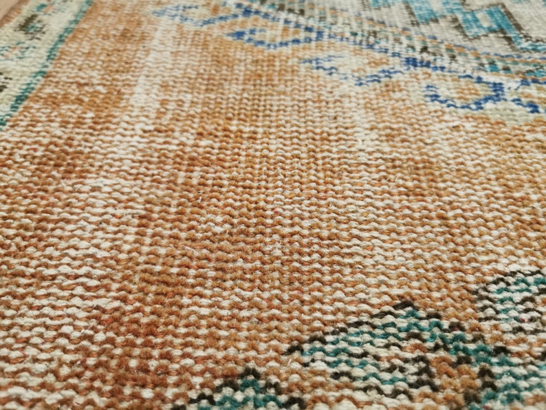 May include: Close-up of a woven rug with a brown, white and blue pattern. The rug has a textured surface and a fringe border.