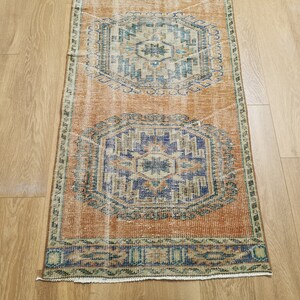 May include: A vintage runner rug with a faded orange background and intricate blue and green patterns. The rug has a fringed edge and is perfect for adding a touch of bohemian style to any room.