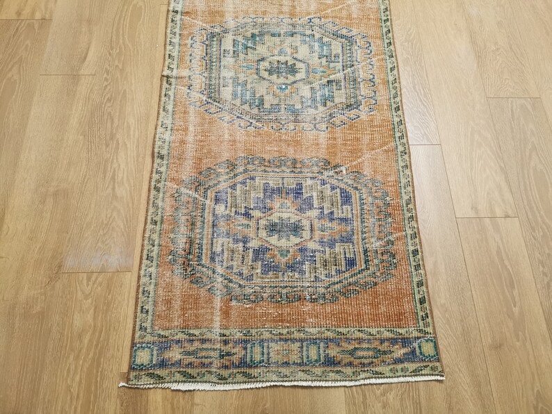 May include: A vintage runner rug with a faded orange background and intricate blue and green patterns. The rug has a fringed edge and is perfect for adding a touch of bohemian style to any room.