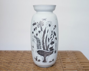 Puede incluir: Jarrón de cerámica blanco con un diseño floral en blanco y negro. El jarrón tiene un cuerpo redondeado y un labio acampanado.