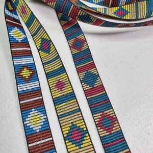 May include: Close-up of colorful woven ribbon with geometric patterns. The ribbon features a repeating design of diamonds and stripes in shades of blue, yellow, red, brown, and white. The ribbon is likely used for crafting or decorative purposes.