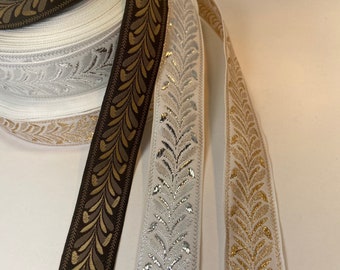 May include: Close-up of decorative ribbon rolls in various colors. The ribbons feature a repeating leaf design in gold, silver, and brown. The rolls are stacked, showcasing the different color options available for crafting and design projects.