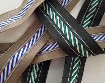 May include: Close-up of several ribbons with striped patterns. One ribbon is tan with blue and white stripes, and another is black with green and white stripes. The ribbons are intertwined, showcasing their textures and designs.