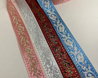 May include: Close-up of decorative ribbon rolls in various colors. The ribbons include pink, silver, red, and blue, each with an ornate, metallic gold or silver design. The ribbons are likely used for crafting, gift wrapping, or embellishments.