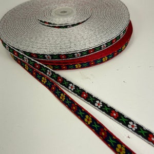 Puede incluir: Carretes de cinta decorativa en rojo, azul marino y gris. Las cintas azul marino y roja presentan un estampado floral con flores rojas, blancas y amarillas. El carrete gris es liso. Ideal para manualidades y adornos.