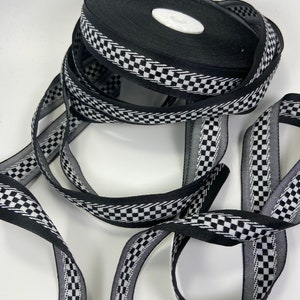 May include: A spool of black ribbon with a checkered white and black border. The ribbon is partially unraveled, displaying the checkered pattern. The ribbon is likely used for crafts, gift wrapping, or decorative purposes.