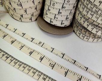 Puede incluir: Primer plano de rollos de cinta métrica blanquecina con marcas negras, que muestran números e incrementos en centímetros. Cinta desenrollada muestra medidas hasta 50 cm. Ideal para proyectos de costura y manualidades.