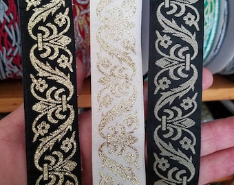 May include: Close-up of three decorative ribbons. The ribbons feature an ornate gold floral design on black, white, and black backgrounds. The ribbons are likely used for embellishments or crafts.