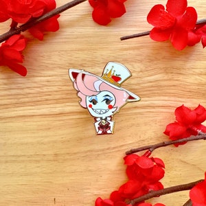 May include: A pink-haired character with a crown and a red and white hat, wearing a red and white shirt with a gold heart, holding a gold heart in their hand. The character is smiling and has a white background.