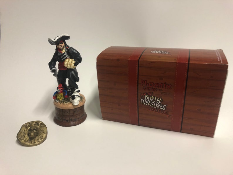 May include: A detailed figurine of a pirate holding a bag of gold coins, standing on a barrel with a parrot and skull. The figurine is part of a Phoenix Comics Buried Treasures collection. The figurine is packaged in a wooden box with the Phoenix Comics logo and the words "Buried Treasures".