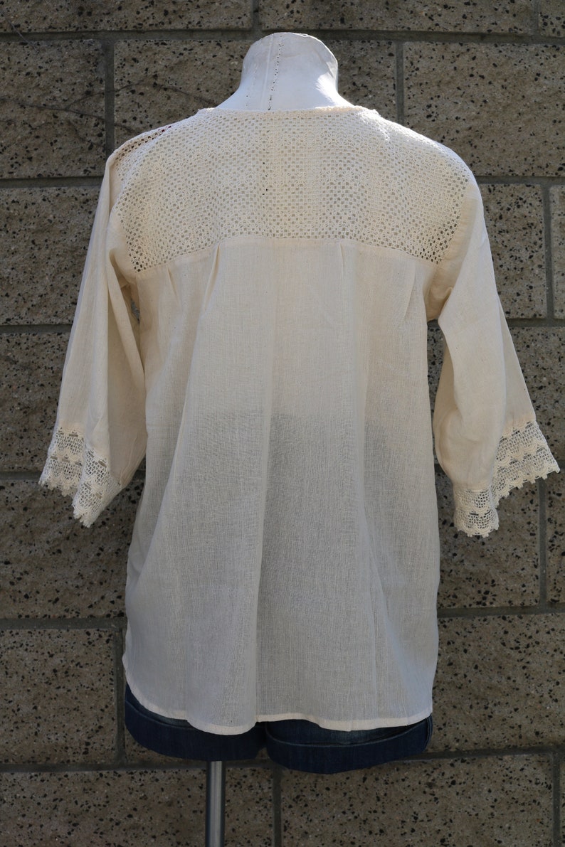 May include: A white crochet top with a lace trim on the sleeves and neckline. The top is made of a lightweight fabric and has a relaxed fit.