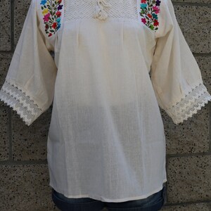 May include: A white cotton blouse with embroidered floral details on the shoulders and lace trim on the sleeves.