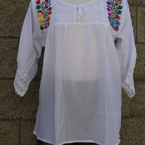May include: White cotton blouse with colourful floral embroidery on the shoulders and a crocheted neckline. The blouse has 3/4 sleeves with crocheted trim.