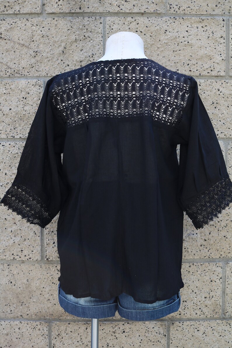 May include: Black crochet top with a lace trim around the neckline and sleeves. The top is made of a lightweight fabric and has a relaxed fit.