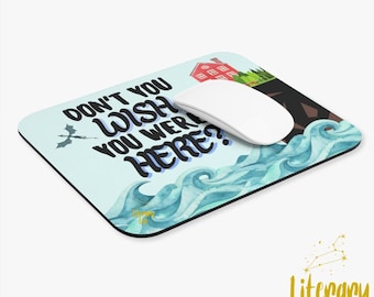 May include: A blue and white mouse pad with a watercolor design of waves and a house on a cliff. The text "Don't you wish you were here?" is written in black on the mouse pad.