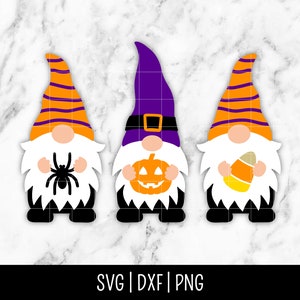 May include: Three Halloween gnomes with orange and purple hats. The gnome on the left is holding a spider, the middle gnome is holding a jack-o-lantern, and the gnome on the right is holding a candy corn.
