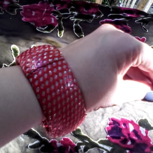 Puede incluir: Un brazalete rojo y blanco de lunares con un acabado brillante.