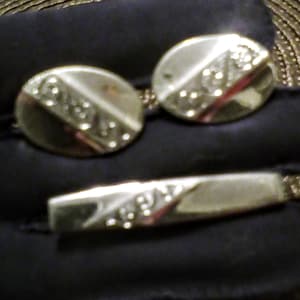 Könnte beinhalten: Ein Set silberner Manschettenknöpfe mit einem dekorativen Design und dem Wort "ROMA" auf jedem Manschettenknopf. Ein silberner Balken mit einem ähnlichen Design und dem Wort "ROMA" ist ebenfalls enthalten.