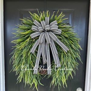 May include: A teardrop-shaped wreath featuring lush, vibrant green fern-like foliage and a large, centered bow made of black and white striped ribbon. The text "Chunka Pookie Creations" is visible in white script across the lower center of the wreath.